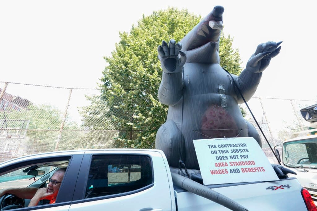 A member of the Carpenters’ Union with an inflatable rat are protesting the contractor building a Shake Shack on the Lower East Side of Manhattan, Thursday, Aug. 4, 2022. On Friday, Aug. 5, the Labor Department delivers its July jobs report. (AP Photo/Mary Altaffer)