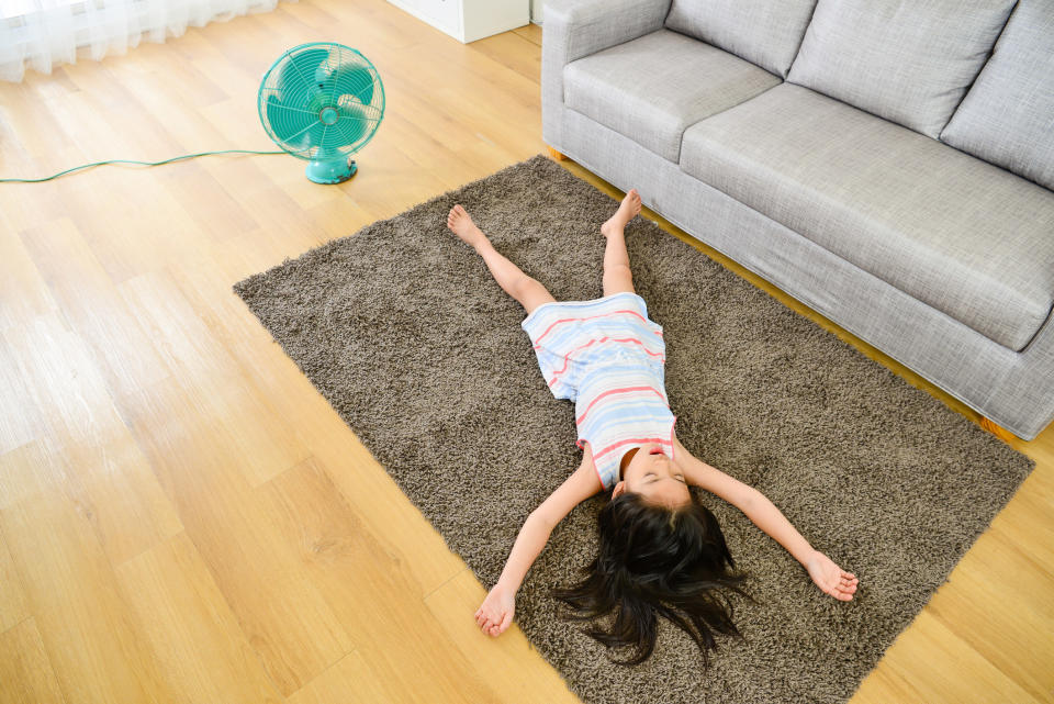 Girl lying down on carpet while electric fan is operating