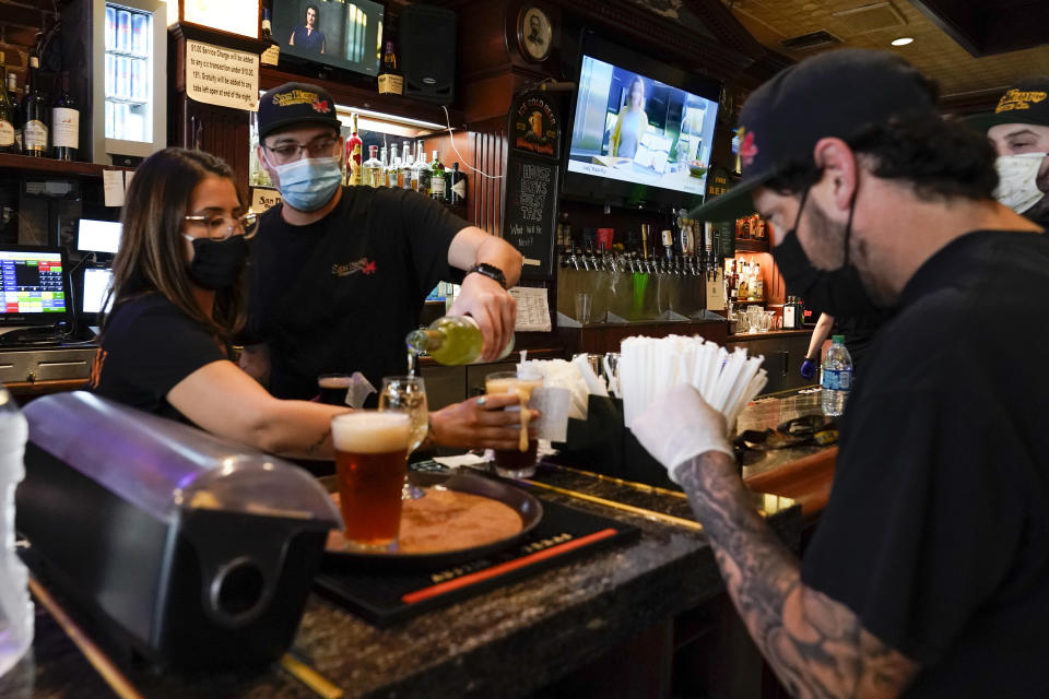 FILE - In this May 29, 2020, file photo, Jessica Ciaramitaro, Daryn Feenstra and Nicholas Soriano mix drinks while wearing face masks at the bar at San Pedro Brewing Company in the San Pedro area of Los Angeles. Coronavirus cases are rising in nearly half the U.S. states, as states are rolling back lockdowns. (AP Photo/Ashley Landis, File)