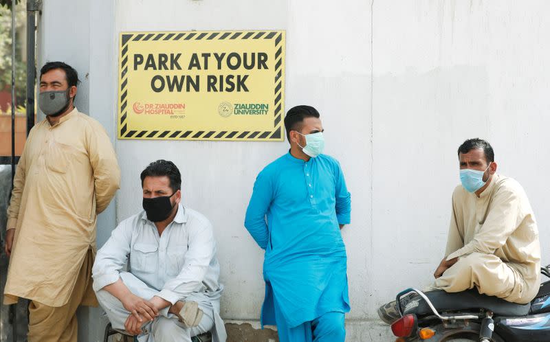 FILE PHOTO: Men wearing face masks wait to see their relatives who were admitted after being affected from a suspected gas leak, at the hospital entrance in Karachi