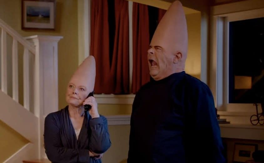 The "coneheads", Mary Margaret and Donald stand in their living room, Mary Margaret is on the phone while Donald pulls a face.