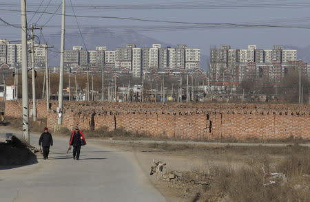 People walk past stacks of bricks in a field near new residential compounds, at a village in Beijing, China, January, 18, 2016. REUTERS/Jason Lee