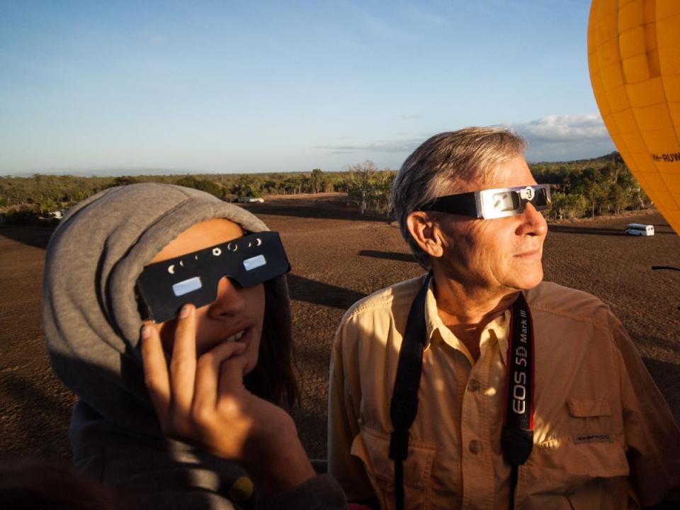 In this photo released by Hot Air Balloon Cairns, Hank Harper, right, of Los Angeles watches the solar eclipse from a hot air balloon near Cairns, Australia, Wednesday, Nov. 14, 2012. Harper flew to Australia with his two children specially to watch the full eclipse, saying we "watched the sun’s rays re-emerge from behind the moon while kangaroos hopped along the ground below." (AP Photo/Hot Air Balloon Cairns)