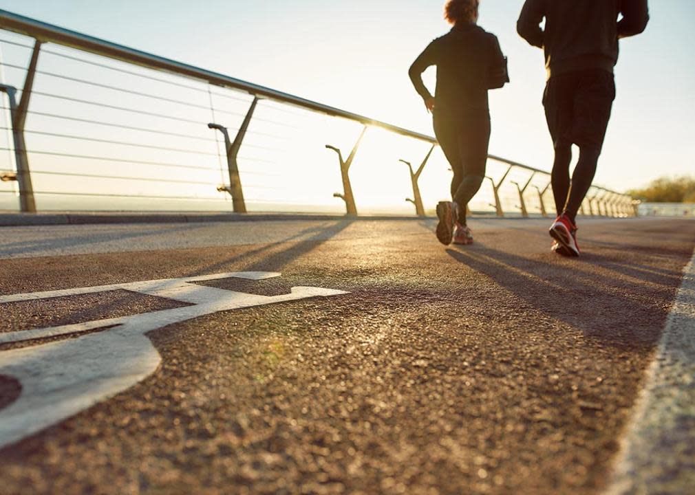 Two people running on the bridge in the morning with a view of sunrise.