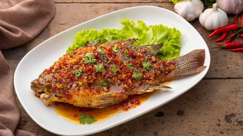 thai spiced whole tilapia on white plate with lettuce leaf
