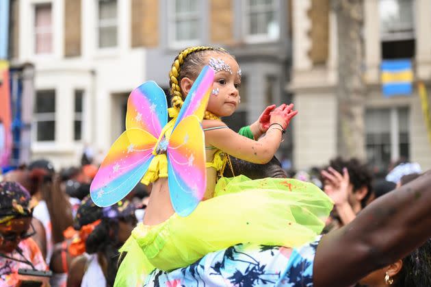 A young girl perched on a man's shoulders wears bright butterfly wings and observes the first day of the Notting Hill Carnival parade. The first Carnival parade is described as family-friendly. (Photo: Clara Watt for HuffPost)
