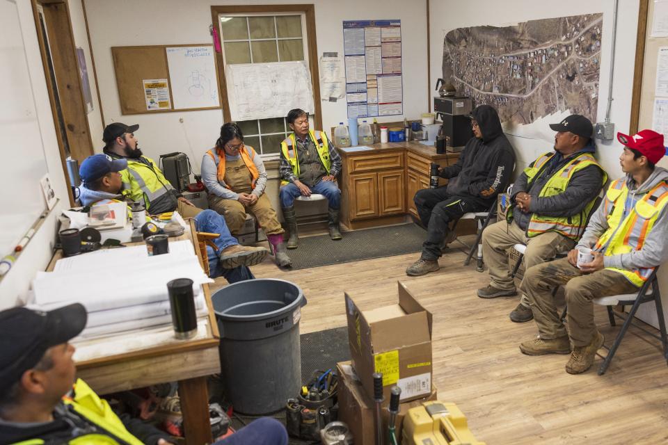 Alaska Native Tribal Health Consortium construction workers listen to Larry Le, center, during a morning meeting, Thursday, Aug. 17, 2023, in Akiachak, Alaska. Most of the village's nearly 700 people are getting modern plumbing for the first time this spring and summer — and finding their lives transformed. (AP Photo/Tom Brenner)