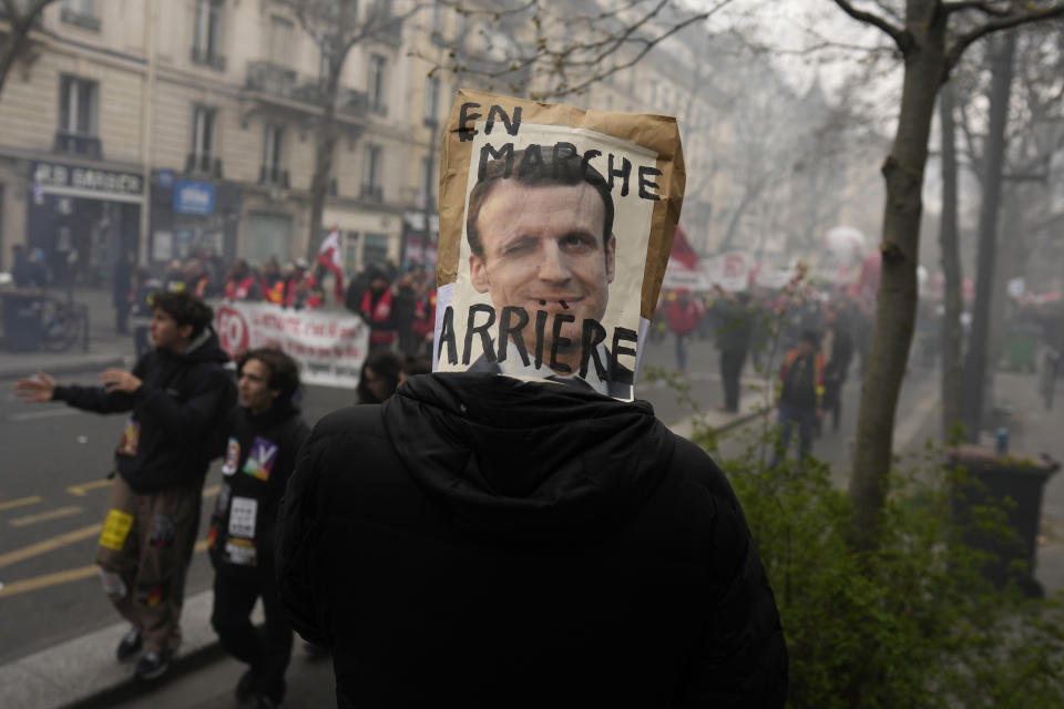 FILE - A demonstrator has a poster mocking French President Emmanuel Macron over his head during a demonstration Tuesday, March 28, 2023 in Paris. With President Emmanuel Macron thousands of miles away in China, French protesters and unions returning to the streets continue to reveal cracks in his domestic political authority. Hundreds of thousands are expected again for the 11th day of nationwide resistance to raising the retirement age from 62 to 64 Thursday, April 6 as the controversial law is being considered by the Constitutional Council. (AP Photo/Thibault Camus, File)