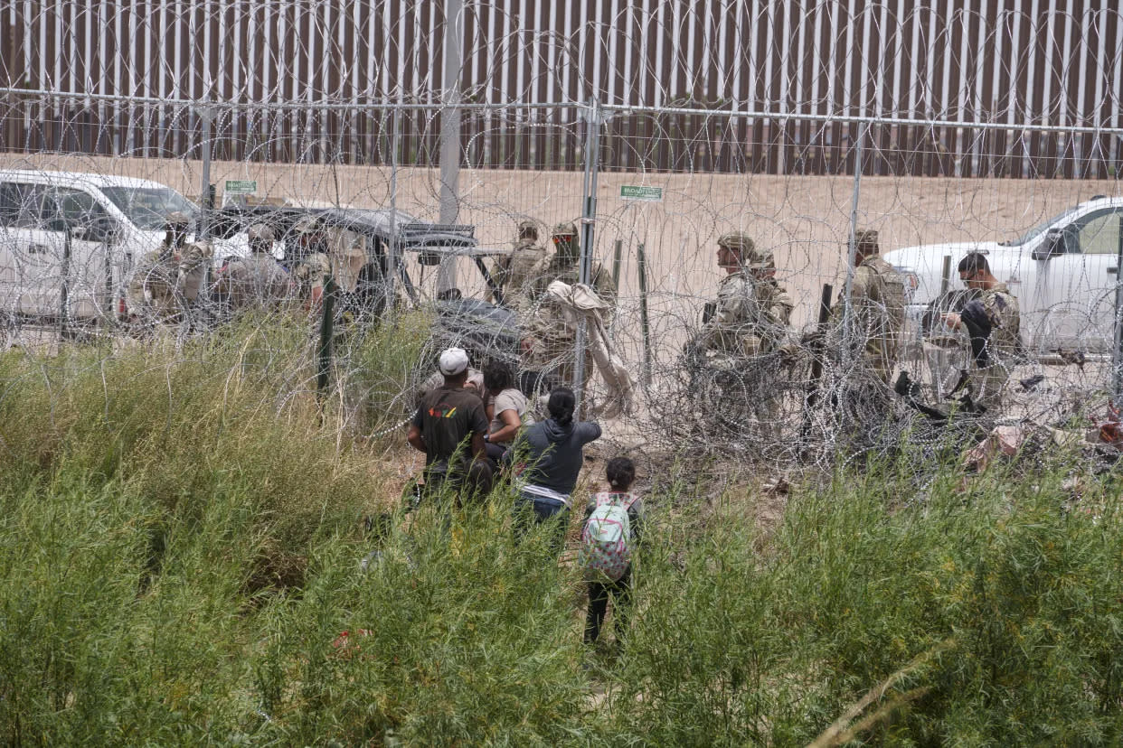 Migrantes hablando con miembros de la Guardia Nacional y la Patrulla de Carreteras de Texas en una valla de concertina en la frontera entre Estados Unidos y México en El Paso, Texas, visto desde Ciudad Juárez, México, el 4 de junio de 2024. (Paul Ratje/The New York Times)
