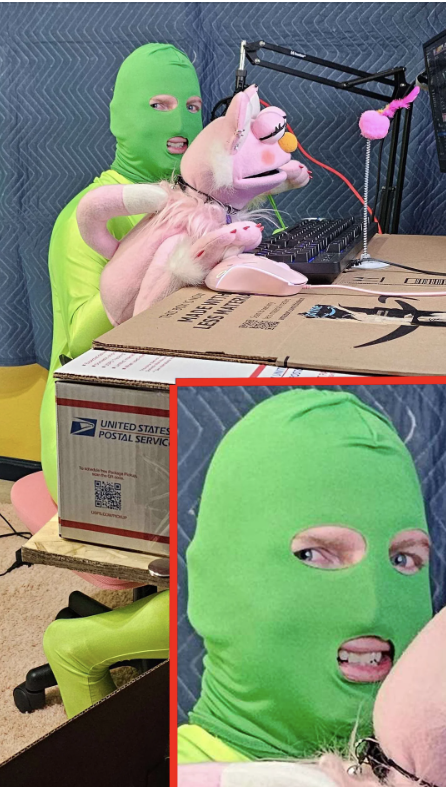 Person in a green spandex suit and balaclava holds a pink unicorn plush while speaking into a microphone at a desk with a cardboard box