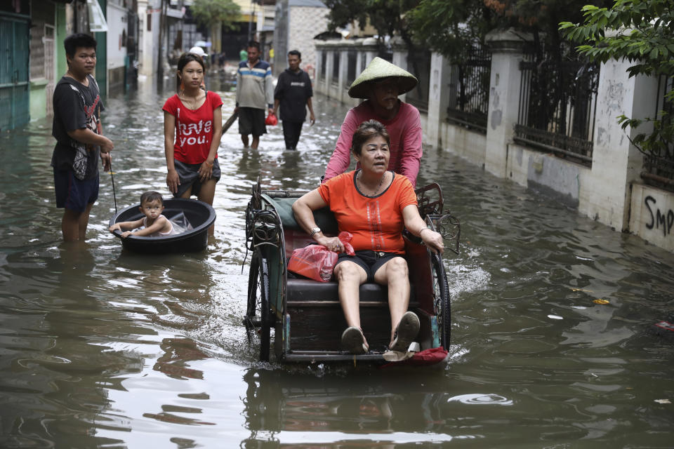 Una mujer cruza una calle anegada sobre un carrito, en Yakarta, Indonesia, el 4 de enero de 2020. (AP Foto/Dita Alangkara)