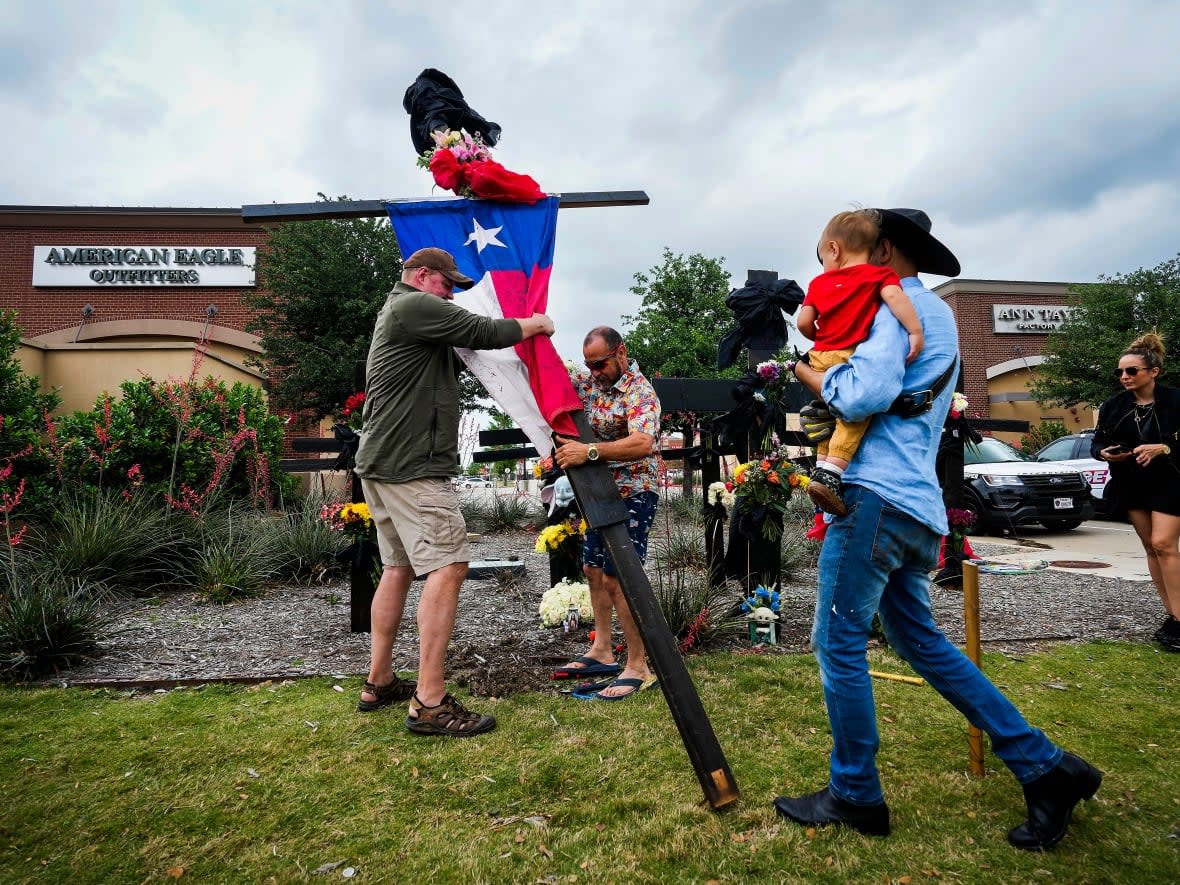 Mourners raise a cross with a Texas flag as they construct a memorial outside an entrance to the mall a day after a mass shooting in Allen, Texas.  (Smiley N. Pool/The Dallas Morning News via AP - image credit)