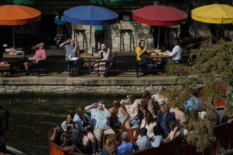 Diners along the Riverwalk and people on a river barge in San Antonio, use special glasses to keep watch as the moon moves in front of the sun during an annular solar eclipse, or ring of fire, Saturday, Oct. 14, 2023. (AP Photo/Eric Gay)