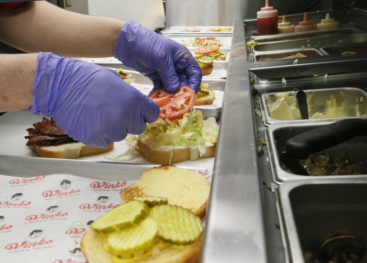 Dylan Pierce dresses a burger in the kitchen at Wink's Drive-In last week.
