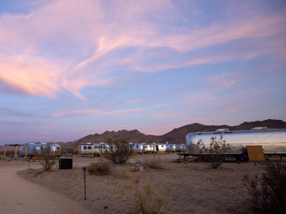 Airstream trailers outside at Autocamp's Joshua Tree location at sunset. There's tables and chairs between each trailer.