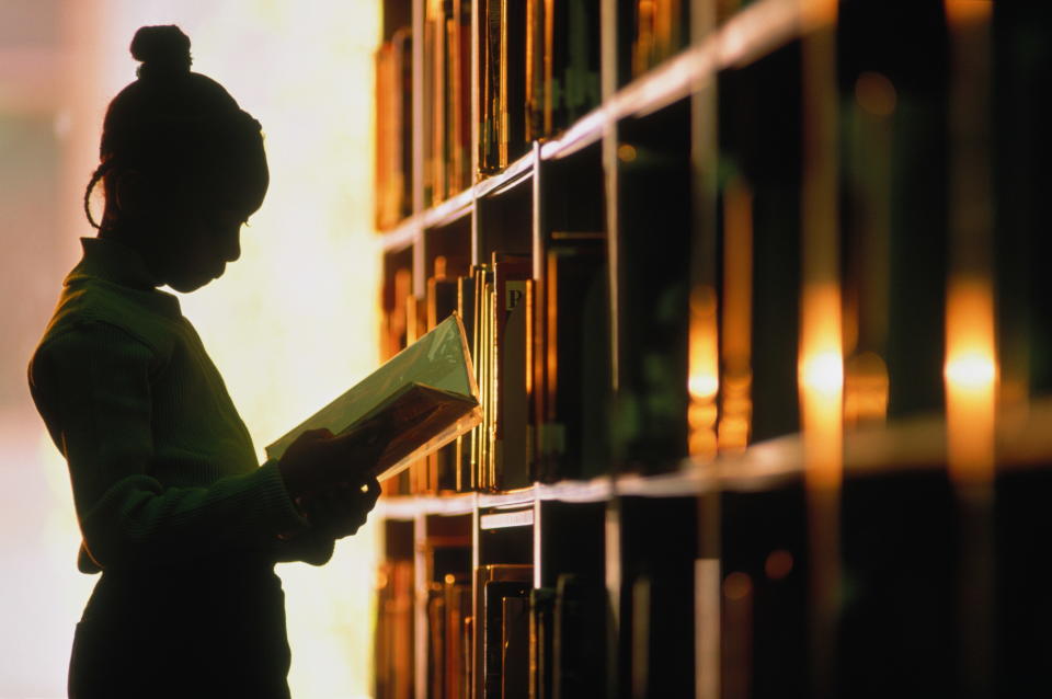 The silhouette of a girl studying in a library aisle