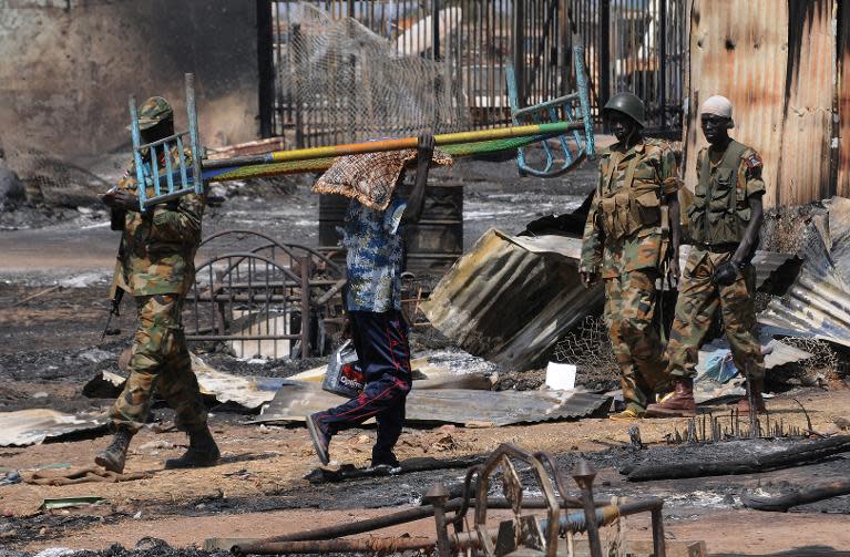 File picture taken on January 12, 2014 shows a man carrying a bed walking past South Sudan People's Liberation Army (SPLA) national army soldiers patrolling the key oil town of Bentiu, South Sudan