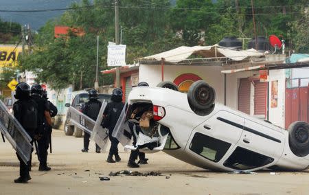 Riot police officers stand guard beside a damaged car after they clashed with protesters from the National Coordination of Education Workers (CNTE) teachers’ union during a protest against President Enrique Pena Nieto's education reform, in the town of Nochixtlan, northwest of the state capital, Oaxaca City, Mexico June 19, 2016. REUTERS/Jorge Luis Plata