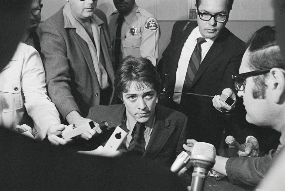 a man in a suit and tie is surrounded by reporters who put microphones near him in a courthouse