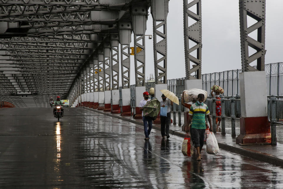 Commuters walk along the city's iconic landmark, Howrah Bridge to cross the Hooghly River as it rains in Kolkata, India, Wednesday, May 20, 2020. Amphan, a powerful cyclone has slammed ashore along the coastline of India and Bangladesh where more than 2.6 million people fled to shelters in a frantic evacuation made all the more challenging by the coronavirus pandemic. (AP Photo/Bikas Das)