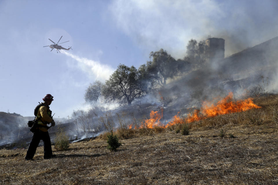 Trinh Nguyen, of the Camarillo Fire Dept, monitors the advance of the Easy Fire as a helicopter makes a water drop Wednesday, Oct. 30, 2019, in Simi Valley, Calif. Driven by powerful Santa Ana winds, the brush fire broke out before dawn between the cities of Simi Valley and Moorpark north of Los Angeles and exploded to more than 1,300 acres (526 hectares), threatening 6,500 homes, Ventura County officials said. (AP Photo/Marcio Jose Sanchez)