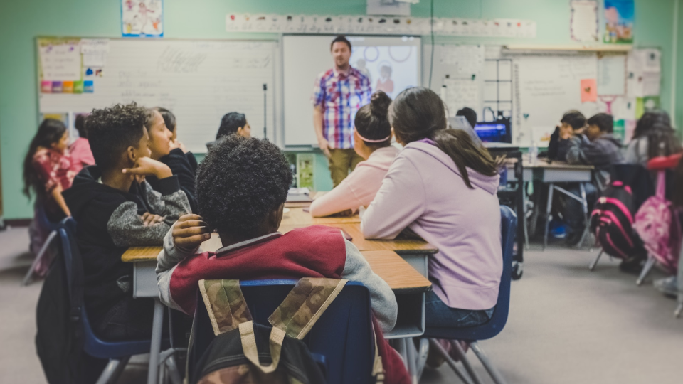 Classroom with students at a desk looking at a teacher