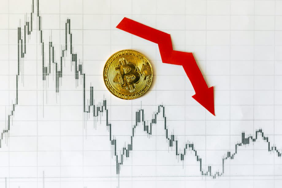 Bitcoin-Münze auf Chart mit rotem Pfeil der abwärts zeigt