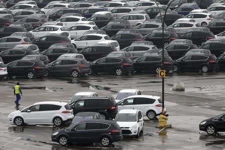 A worker walks by Ford vehicles in a parking lot at the Ford assembly plant in Genk December 17, 2014. REUTERS/Francois Lenoir