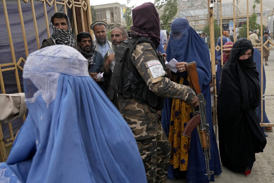 FILE - A Taliban fighter stands guard as people wait to receive food rations distributed by a South Korean humanitarian aid group, in Kabul, Afghanistan, May 10, 2022. (AP Photo/Ebrahim Noroozi, File)