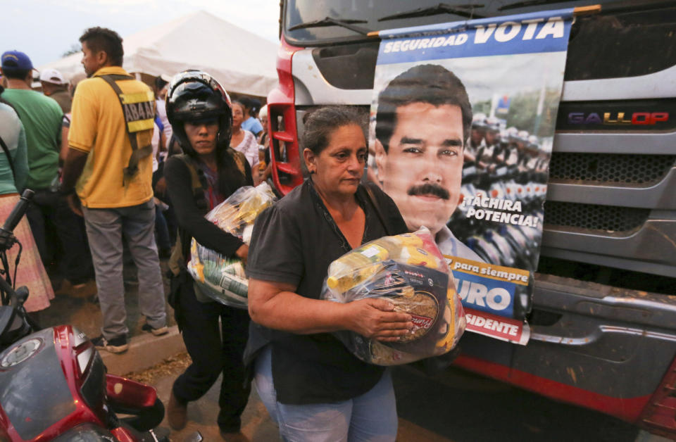 People carry bags with food provided by the Nicolas Maduro's government near the international bridge of Tienditas on the outskirts of Urena, Venezuela, Monday, Feb. 11, 2019. Nearly three weeks after the Trump administration backed an all-out effort to force out President Nicolas Maduro, the embattled socialist leader is holding strong and defying predictions of an imminent demise. (AP Photo/Fernando Llano)