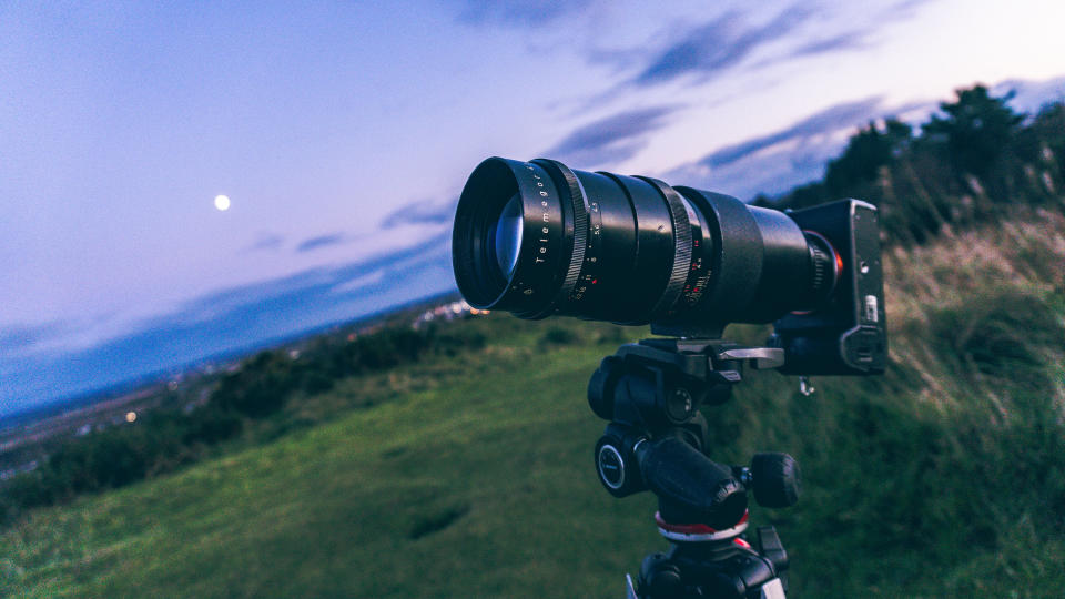 Camera deals: Image shows camera with lens attached,. It's dusk and a field and darkening sky are visible behind the camera.