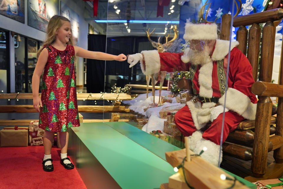 Sydney Poulos, 8, gives Santa a fist bump through a transparent barrier at a Bass Pro Shop in Bridgeport, Conn., Tuesday, Nov. 10, 2020. Santa Claus is coming to the mall — just don't try to sit on his lap. Malls are doing all they can to keep the jolly old man safe from the coronavirus, including banning kids from sitting on his knee, no matter if they've been naughty or nice. (AP Photo/Seth Wenig)