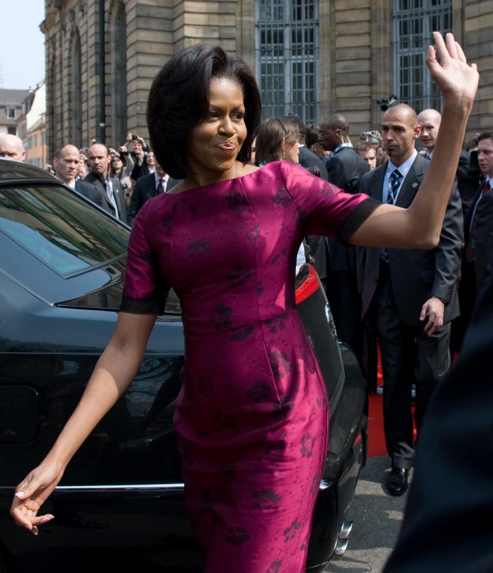 Michelle Obama waves, wearing a pink dress.