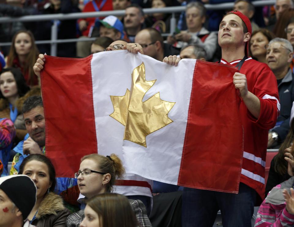 Fans raise a Canadian flag featuring a gold maple leaf as they watch the men's preliminary round ice hockey game between Canada and Norway at the Sochi 2014 Sochi Winter Olympics, February 13, 2014. REUTERS/Gary Hershorn (RUSSIA - Tags: OLYMPICS SPORT ICE HOCKEY)