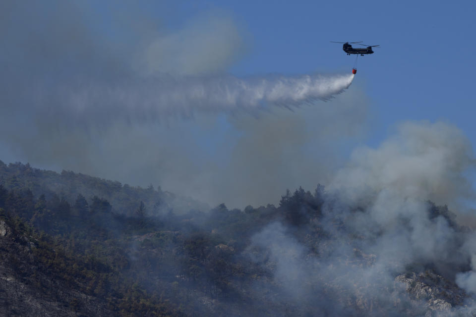 A chinook military helicopter drops water on a fire during a wildfire near Malakasa, in northern Athens, Greece, Saturday, Aug. 7, 2021. Wildfires rampaged through massive swathes of Greece's last remaining forests for yet another day Saturday, encroaching on inhabited areas and burning scores of homes, businesses and farmland. (AP Photo/Petros Karadjias)