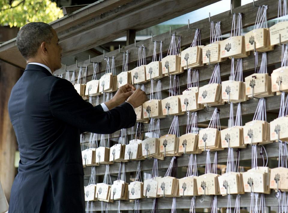 President Barack Obama places a prayer tablet on the Votive Tree as he tours Meiji Shrine in Tokyo, Thursday, April 24, 2014. Showing solidarity with Japan, Obama affirmed Thursday that the U.S. would be obligated to defend Tokyo in a confrontation with Beijing over a set of disputed islands, but urged all sides to resolve the long-running dispute peacefully. (AP Photo/Carolyn Kaster)