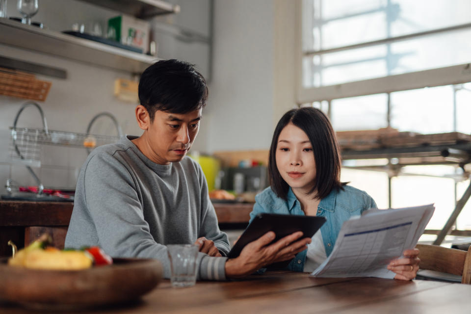Young Asian couple making financial bills payment via electronic banking on iPad. Managing taxes and financial bills. Dealing with inflation. Mortgage loan payment. Finance and technology.