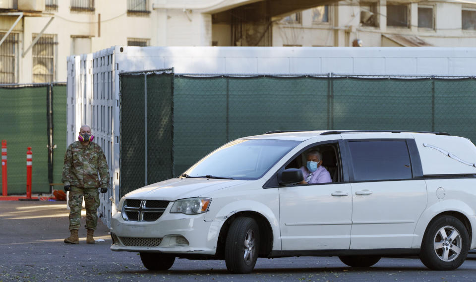 A member of the California National Guard stands next to refrigerated trailers as a funeral hearse driver exits the department of the Los Angeles County Coroner in Los Angeles, Monday, Jan. 11, 2021. The coronavirus death toll in California reached 30,000 on Monday, another staggering milestone as the nation's most populous state endures the worst surge of the nearly yearlong pandemic. (AP Photo/Damian Dovarganes)