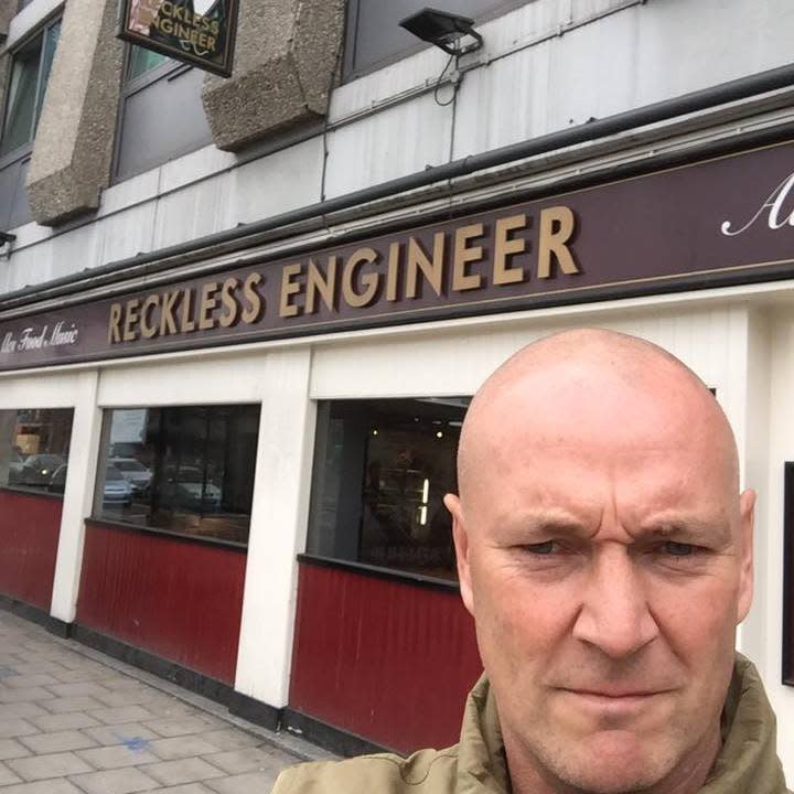 Malcolm Callender in front of a building that says 'Reckless Engineer' on it. 