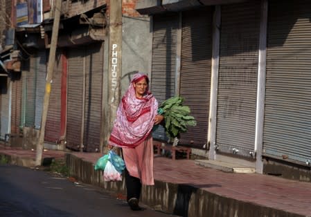 A woman carrying eatables walks past closed shops during restrictions after the government scrapped special status for Kashmir, in Srinagar