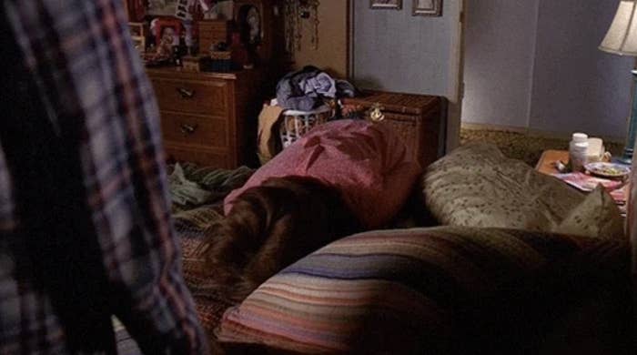 A person is seen lying face down on a bed in a messy room with a dresser, clothing and pillows visible.  The setting suggests a relaxed and personal atmosphere.