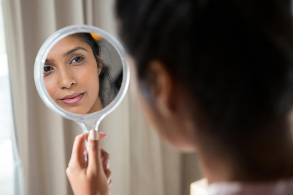 woman looking at her reflection in a hand mirror