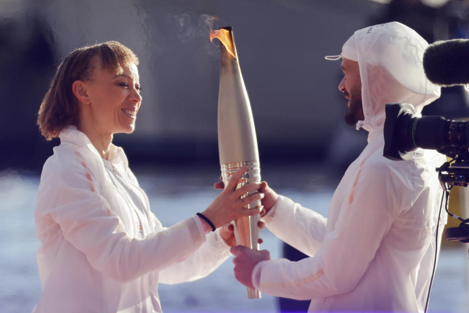 French Paralympic athlete Nantenin Keïta, left, passes the Olympic torch to French rap artist Jul during the torch arrival ceremony in Marseille, southern France, Wednesday May 8, 2024. After leaving Marseille, a vast relay route is undertaken before the torch odyssey ends on July 27 in Paris. The Paris 2024 Olympic Games will run from July 26 to Aug.11, 2024. Keita is visually impaired and won a gold medal during the 2016 Olympics in Rio de Janeiro. (Ludovic Marin, Pool via AP)