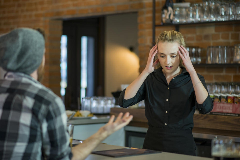 A person in a black shirt appears stressed, hands on head, facing another gesturing person