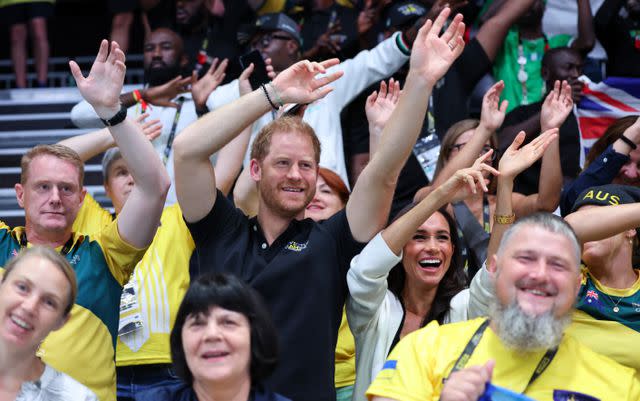 <p>Chris Jackson/Getty</p> Prince Harry and Meghan Markle wave their hands as they attend the wheelchair basketball game between Ukraine and Australia