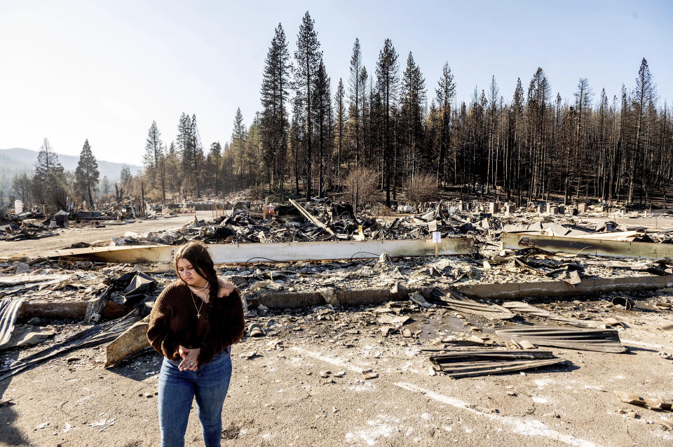 Kyra Cedillos, 14, stands in front of the remains of Hunter Ace Hardware, destroyed by the Dixie Fire, in the Greenville community of Plumas County, Calif., on Sunday, Sept. 5, 2021. Cedillos was helping grandmother Kimberly Price feed cats left behind by Dixie Fire evacuees. (AP Photo/Noah Berger)