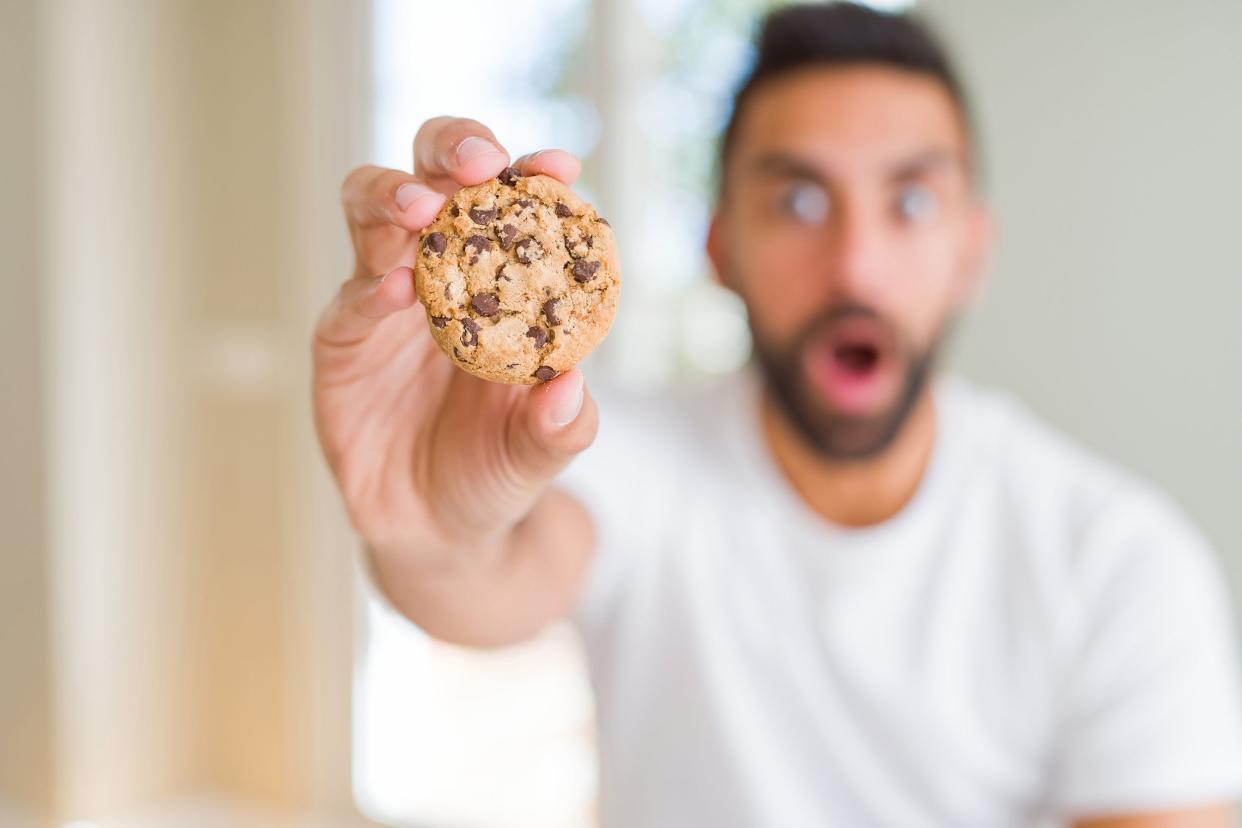 hispanic man eating chocolate chips cookies scared in shock with a surprise face