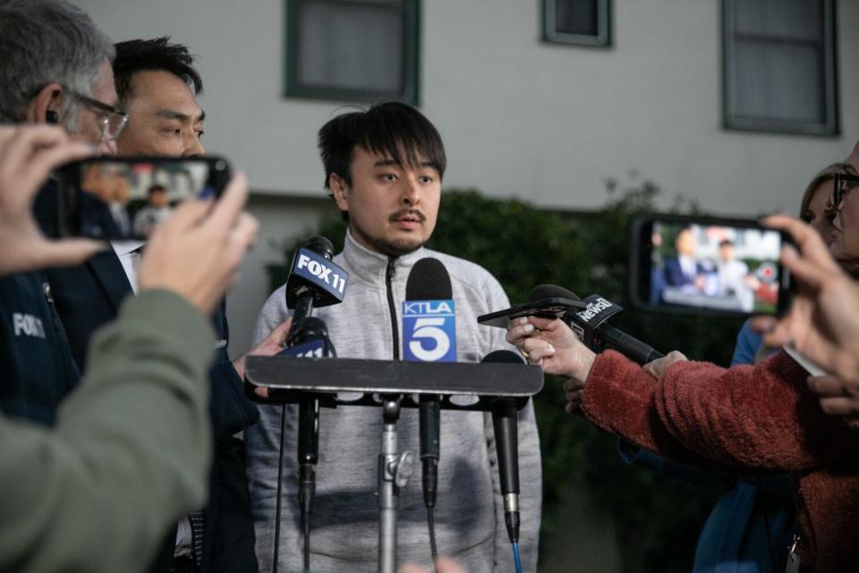 A man stands before a bank of microphones in front of reporters.