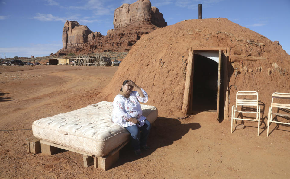 In this Thursday, Oct. 25, 2018, photo, Navajo Julie Ann Holiday sits on a mattress in front of her traditional Navajo dwelling made of wood caulked with earth, in Monument Valley, Utah. The circular Hogan she shares with her husband is one room with a dirt floor, heated with a wood stove. She loves waking up to the view of formations like Bear and Rabbit in the distance, and in the warmer months she and her husband sleeps outside on a mattress under the stars. (AP Photo/Rick Bowmer)