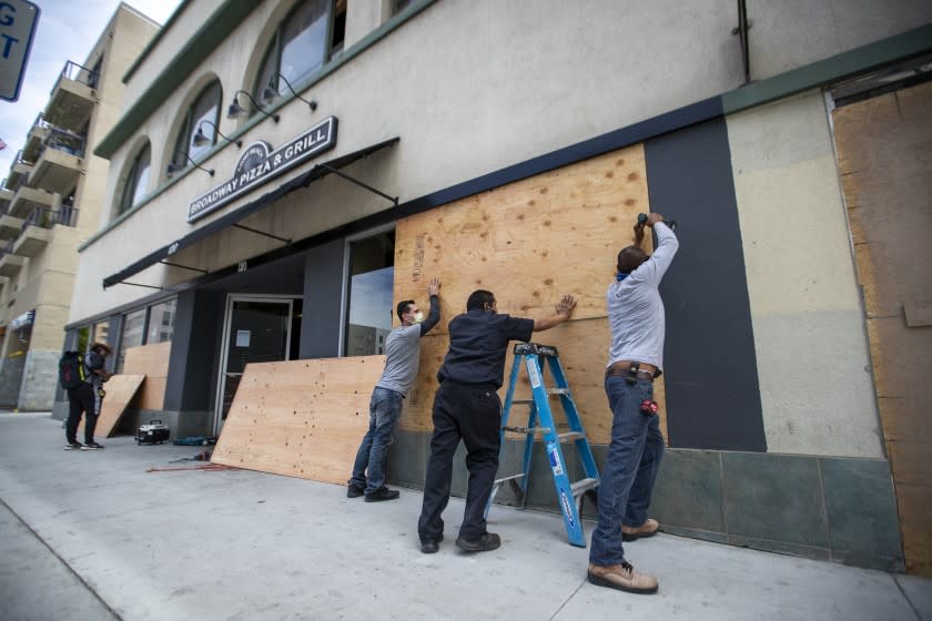 LONG BEACH, CA - JUNE 01: After rioters looted, destroyed and burned businesses along Pine Ave. Sunday evening, a worker puts up sheets of plywood over windows of a business while California National Guard members patrol the streets Monday, June 1, 2020 in Long Beach, CA. (Allen J. Schaben / Los Angeles Times)